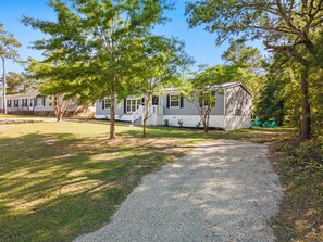 A single-story house with a gravel driveway, surrounded by trees and a grassy lawn. - Coastal 3BR w/Game Room, 5 mins to beach, FirePit (Shallotte)