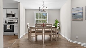 Une cuisine moderne avec des meubles blancs, un four à micro-ondes et une cuisinière. On y trouve une table à manger avec des chaises et un luminaire suspendu.