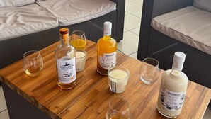 A wooden coffee table with bottles of Montebello Punch Coco and Habitat Barrel Honey, two glasses, and a candle. - Villa LOMA, overlooking lush garden and private pool. Ideal for 8 people. (Sainte-Rose)