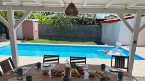 A covered outdoor dining area with a pool in the background. - Villa LOMA, overlooking lush garden and private pool. Ideal for 8 people. (Sainte-Rose)