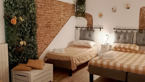 A bedroom with two beds, a brick wall, and a green wall with plants. - Three-bed vacation home in the city of the Leaning Tower (Pisa)