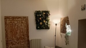 A dining area with a wooden table, a sofa, and a chair. There is a wall-mounted flower arrangement and a wall with a brick texture. - Three-bed vacation home in the city of the Leaning Tower (Pisa)