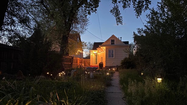 Un chemin menant à une maison décorée de guirlandes lumineuses et entourée d’une clôture en bois.