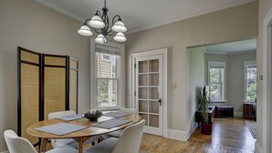 Un coin repas avec une table ronde, des chaises et un lustre. Il y a des portes coulissantes et une vue sur l’extérieur.