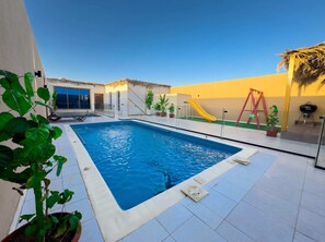 Una piscina con tobogán, zona de barbacoa y área de juegos.