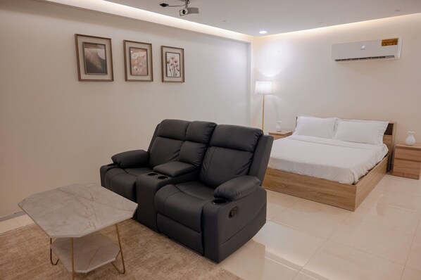 Un dormitorio moderno con una butaca reclinable, una cama, una mesita de noche y una lámpara.