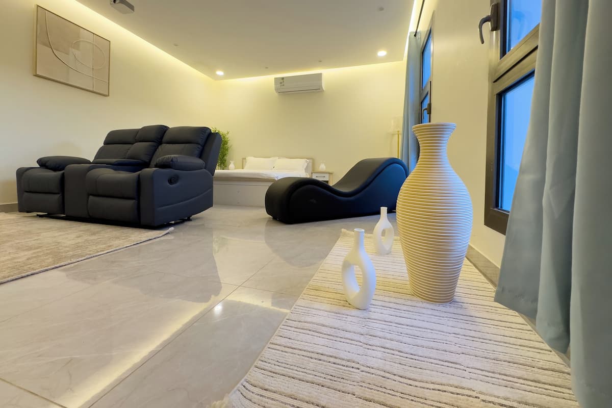 A modern living room with a reclining chair, a sofa, a large vase, and a window with curtains.