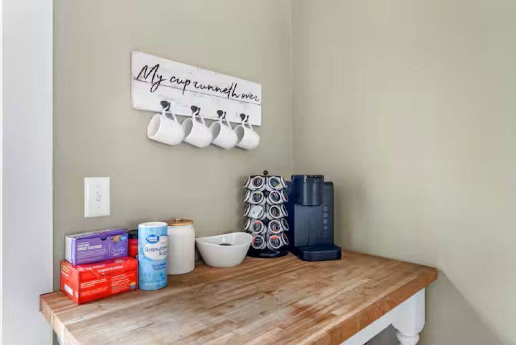 Una encimera de cocina con una cafetera, un fajo de toallas de papel, una caja de pañuelos, un tazón y un cartel en la pared.