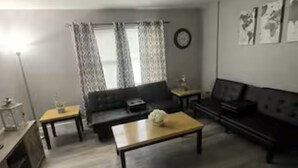A living room with a sofa, coffee table, and a TV. There are curtains on the window and a lamp on the left. - Spacious 3 Bedroom (Cary)