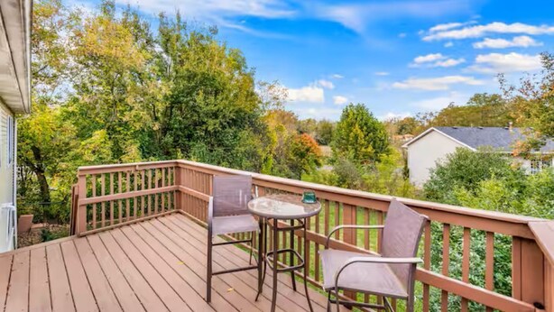 A wooden deck with a table and chairs, surrounded by lush greenery and trees. - Spacious 3 Bedroom (Cary)