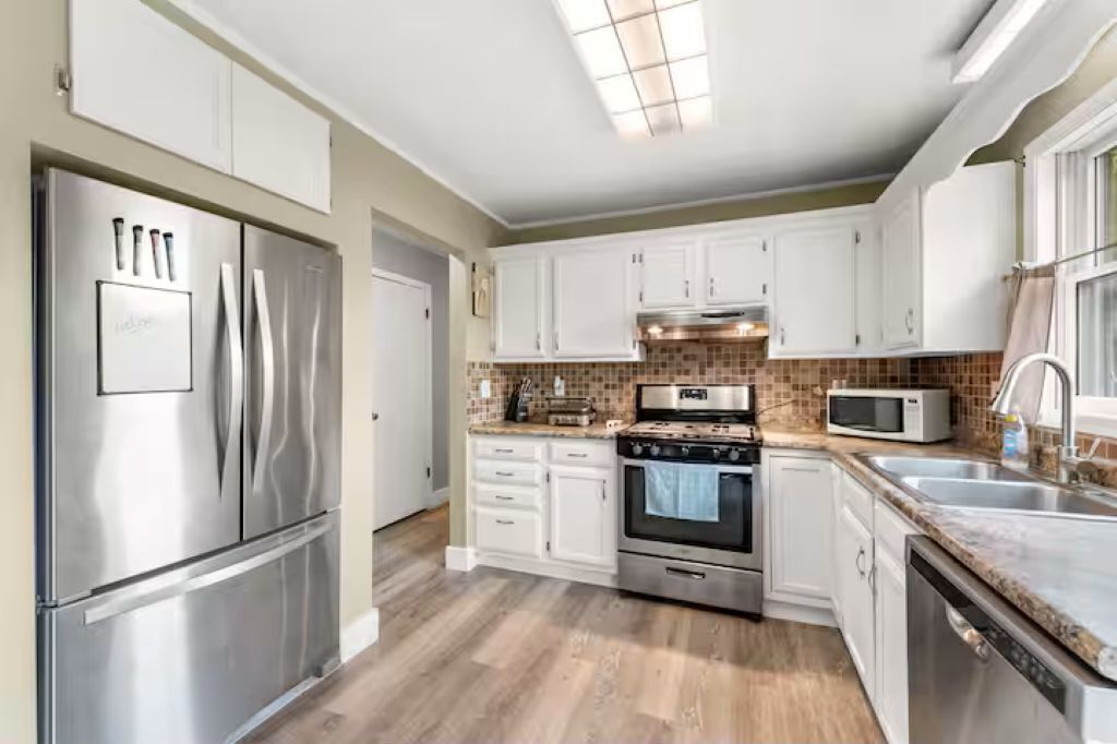 A modern kitchen with white cabinets, stainless steel appliances, and a tiled backsplash.