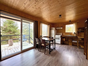 A wooden cabin interior with a dining area, kitchen, and large sliding glass doors leading to a deck.