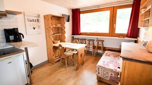 A compact kitchen with a wooden table, stools, a coffee machine, and a window with curtains. - Studio for 3/4 People - LA Meije - 013me - Plagne Centre (La Plagne-Tarentaise)