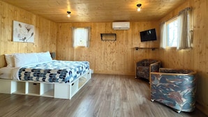 Ein Zimmer mit Holzvertäfelung, einem Bett, einem Fernseher und einer kleinen Sitzecke.