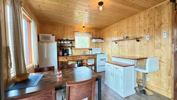 Een keuken met houten lambrisering, een eettafel, stoelen, een magnetron, een fornuis en een klein barretje.