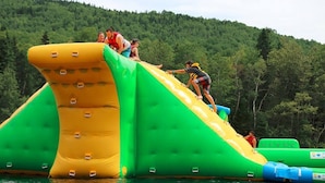 Eine aufblasbare Wasserrutsche mit grün-gelbem Design vor einer bewaldeten Hügellandschaft.