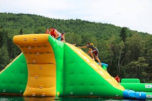 Un tobogan aquàtic inflable amb disseny verd i groc, situat davant d'un turó boscós.