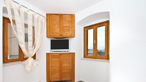 A small room with a bed, a TV, wooden cabinets, and two windows. - Apartment Center Marija best location (Vodice)