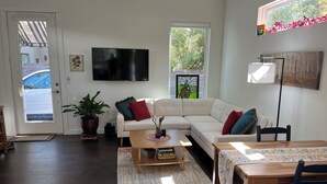 Een woonkamer met een witte bank, een salontafel, een televisie en een raam met uitzicht op bomen.