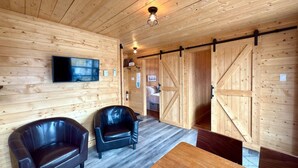 A wooden interior with two leather chairs, a wooden table, and a TV mounted on the wall. - Mini-chalet#7- Un pur ressourcement - Pohénégamook (Pohenegamook)