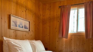 A wooden cabin bedroom with a bed, a window with curtains, and a framed picture on the wall. - Mini-chalet#7- Un pur ressourcement - Pohénégamook (Pohenegamook)