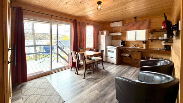 A wooden cabin with a dining area, kitchen, and a sliding glass door leading to a deck. - Mini-chalet#7- Un pur ressourcement - Pohénégamook (Pohenegamook)
