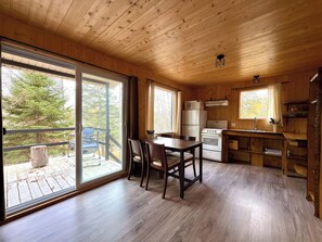 Interior de una cabaña de madera con comedor, cocina y grandes puertas corredizas de vidrio que dan a una terraza.