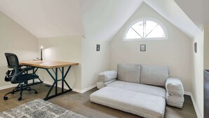 Ett rum i loftstil med ett skrivbord i trä, en svart kontorsstol, en grå soffa och ett litet fönster.