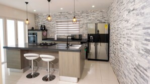 Una cocina moderna con una isla central, luces colgantes y un salpicadero de piedra.