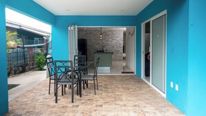 Un patio con una mesa y sillas, suelo de piedra y vista hacia una zona de cocina con salpicadero de piedra.