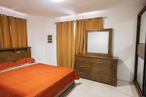 Une chambre à coucher avec un lit, une commode en bois, un miroir et des rideaux.
