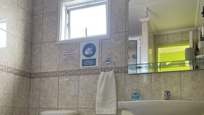 A bathroom with a toilet, sink, and a small trash bin. There is a window providing natural light and a mirror above the sink. - Casa lucy bed and breakfast. Familiar, comfortable, near to Natales center. (Puerto Natales)