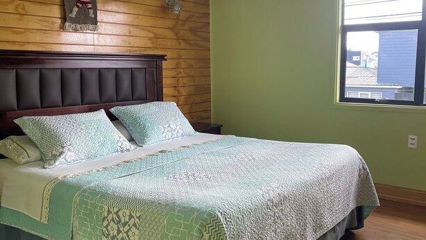 A bedroom with a wooden headboard, a patterned bedspread, and a window with a view of buildings. - Casa lucy bed and breakfast. Familiar, comfortable, near to Natales center. (Puerto Natales)