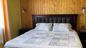A neatly made bed with a quilted cover, wooden paneling on the walls, and two bedside lamps.