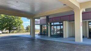 Uma área externa coberta com um caminho pavimentado, entrada de vidro e varanda com guarda-corpo roxo.