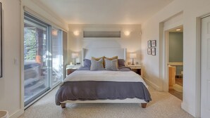 A bedroom with a large bed, a sliding glass door, and a small bathroom visible through an open door. - Ski-in/out spacious 3BR Saddle Ridge townhome, steps to Ironhorse Lift & hot tub (Big Sky)