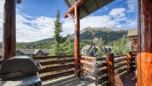 A wooden deck with a grill and a chair, overlooking a mountainous landscape with houses. - Ski-in/out spacious 3BR Saddle Ridge townhome, steps to Ironhorse Lift & hot tub (Big Sky)