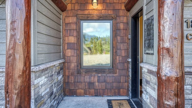 A wooden exterior with a framed window and a door, a stone base, and a doormat. - Ski-in/out spacious 3BR Saddle Ridge townhome, steps to Ironhorse Lift & hot tub (Big Sky)