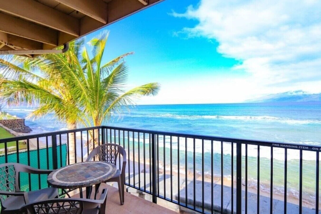 A balcony with a view of the ocean, a palm tree, and a table with chairs.