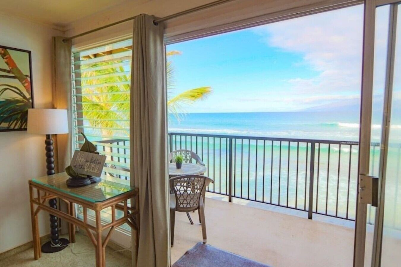 A room with a glass table, a chair, a small table with a sign, and a view of the ocean through a balcony.