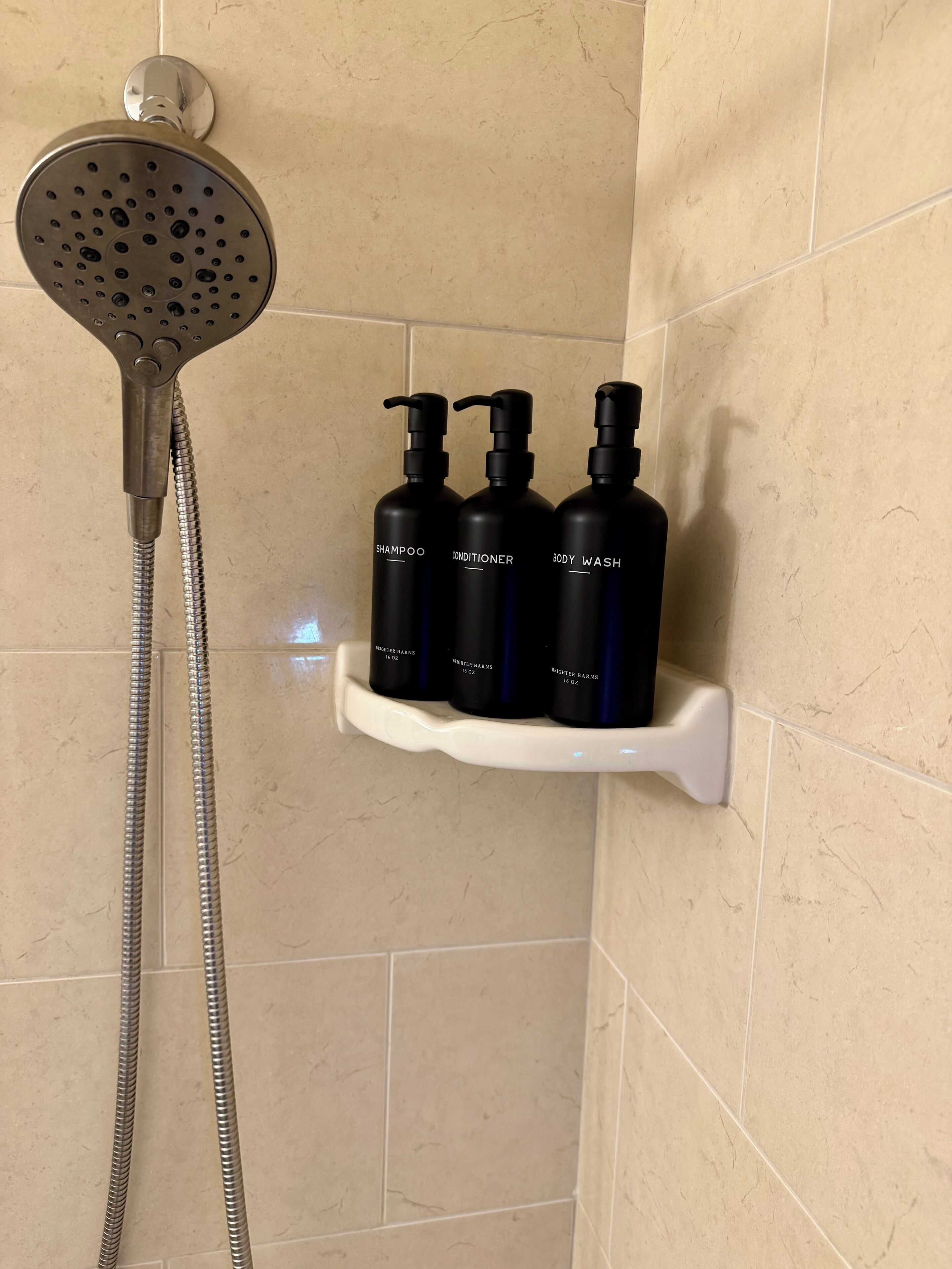 Ducha con cabezal de ducha de mano y estante adosado a la pared que sostiene tres botellas de jabón corporal y acondicionador.