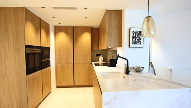 A modern kitchen with wooden cabinets, a black oven, a marble countertop, and a pendant light. - Apartment on Croisette Near Palm Beach (Cannes)