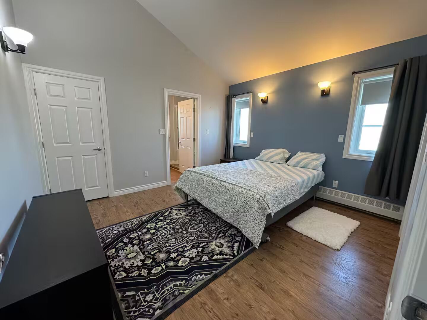 Un dormitorio con cama, alfombra, escritorio y ventana con cortinas.