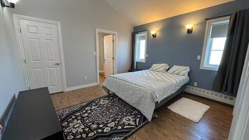 Un dormitorio con cama, alfombra, escritorio y ventana con cortinas.