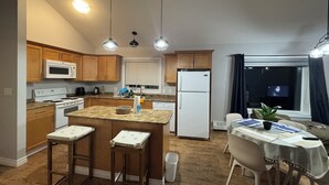 Una cocina moderna con armarios de madera, un refrigerador blanco, un microondas y una zona de comedor con una mesa y sillas.