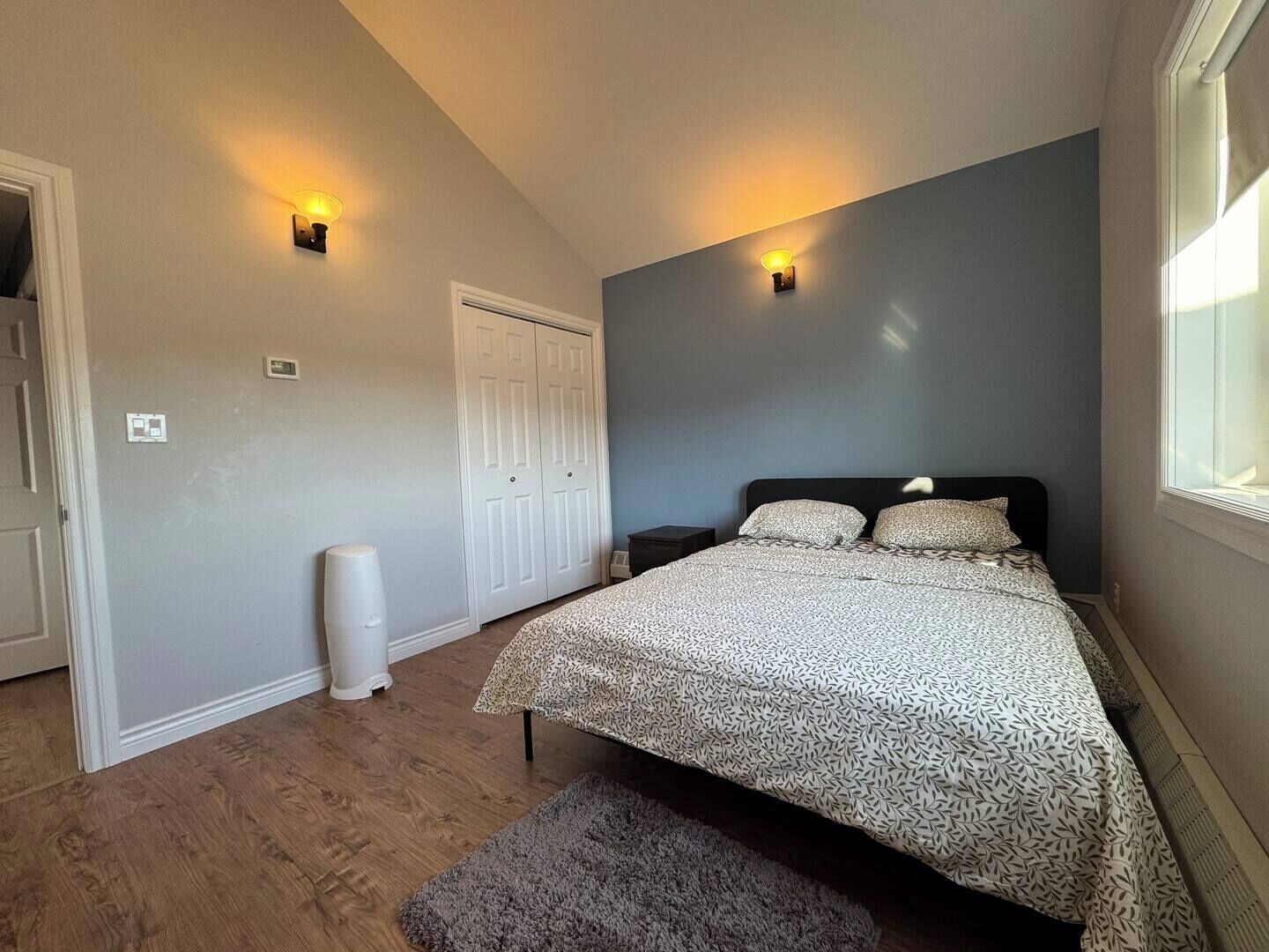Ein Schlafzimmer mit einem Bett, zwei Wandleuchten, einer weißen Tür und einem Fenster.