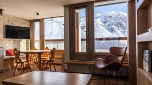 Un interior moderno con pared de piedra, muebles de madera y amplios ventanales que ofrecen vistas a una montaña nevada.