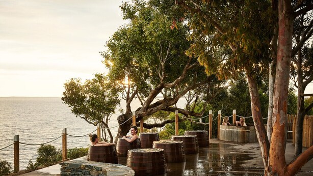 A waterfront deck with wooden barrels, a stone wall, and a wooden fence. - Parachilna at Boardwalk Villas Metung (Metung)