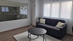 A modern living room with a dark sofa, a round table, a tall floor lamp, and a large window with sheer curtains. - Gîte Un instant de rêve in Dorlisheim, heated indoor pool, sauna (Dorlisheim)