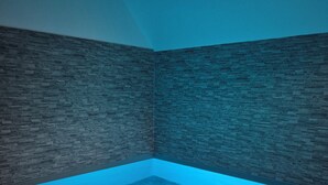 A room with a blue-lit pool, stone walls, and a wooden floor. - Gîte Un instant de rêve in Dorlisheim, heated indoor pool, sauna (Dorlisheim)